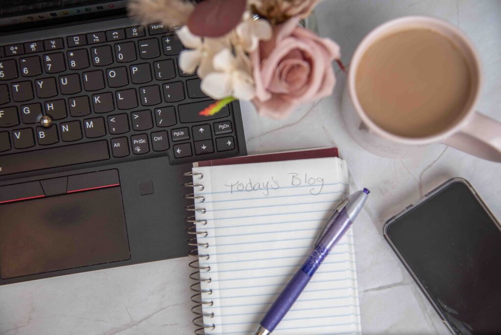 computer keyboard with notepad, coffee mug pen and smartphone on a table with flowers