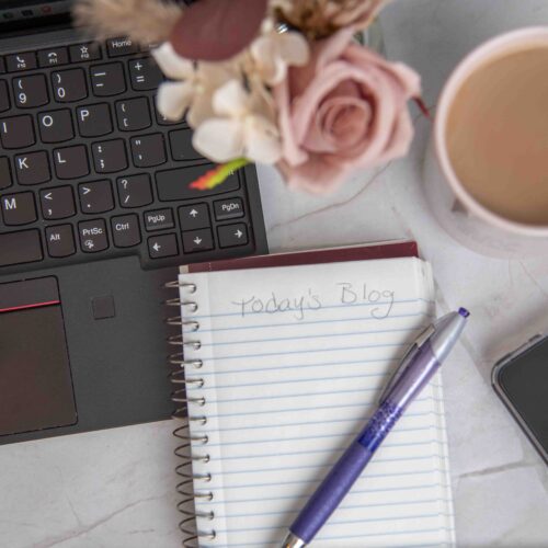 computer keyboard with notepad, coffee mug pen and smartphone on a table with flowers