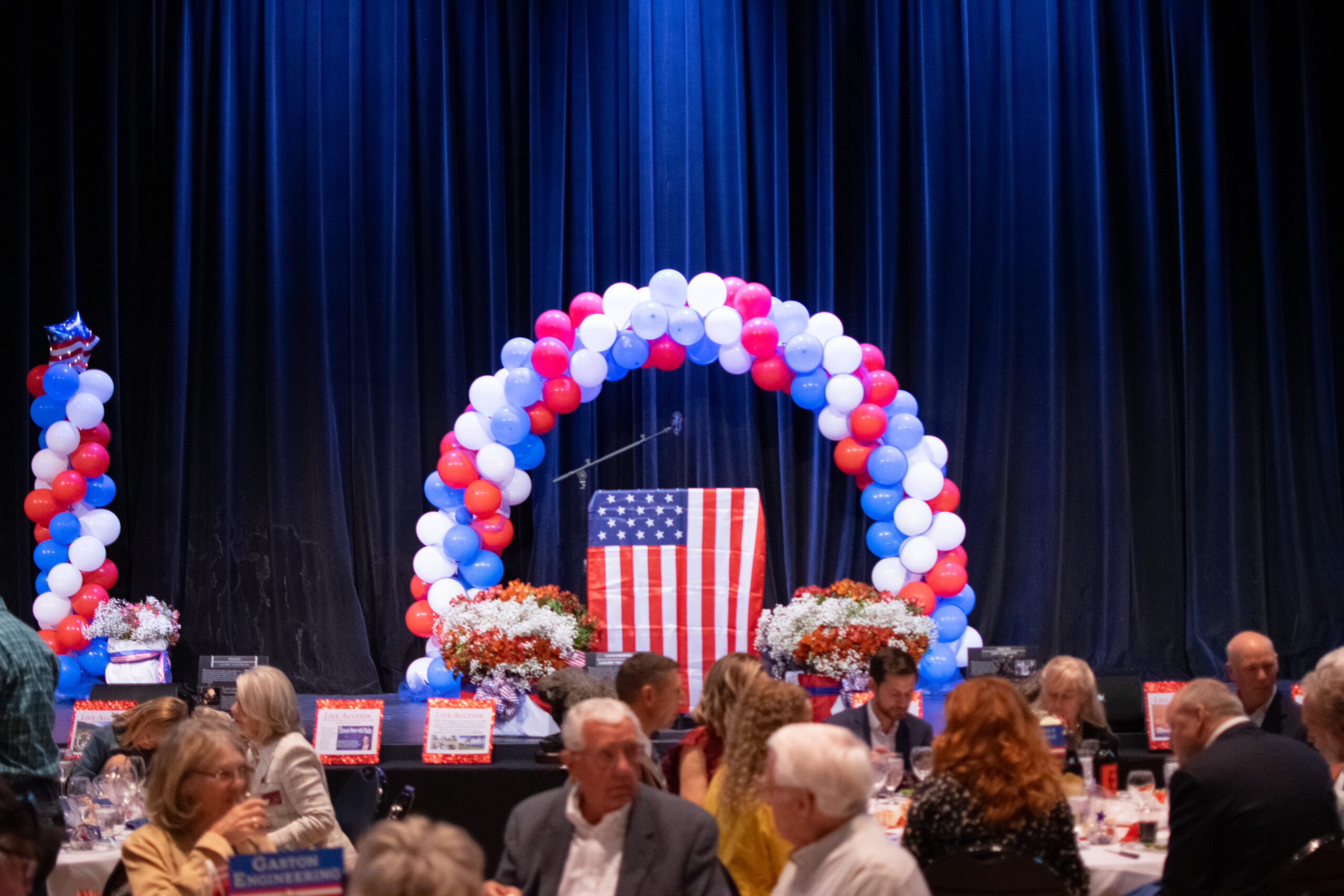 event stage with American flag and people conversing below