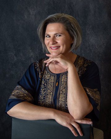 Woman smiling in dark blue shirt with gold details